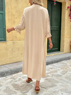 Elegant beige button-front maxi dress with long sleeves and flowing silhouette.