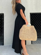 Woman wearing a flowing black deep V-neck maxi dress with side slit and relaxed elegant silhouette.