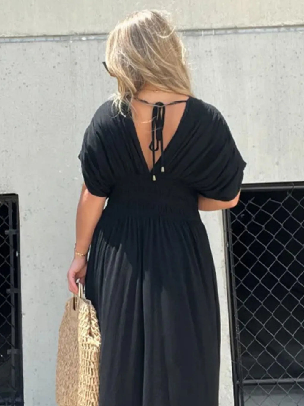 Woman wearing a flowing black deep V-neck maxi dress with side slit and relaxed elegant silhouette.