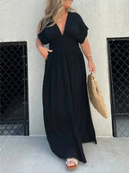 Woman wearing a flowing black deep V-neck maxi dress with side slit and relaxed elegant silhouette.