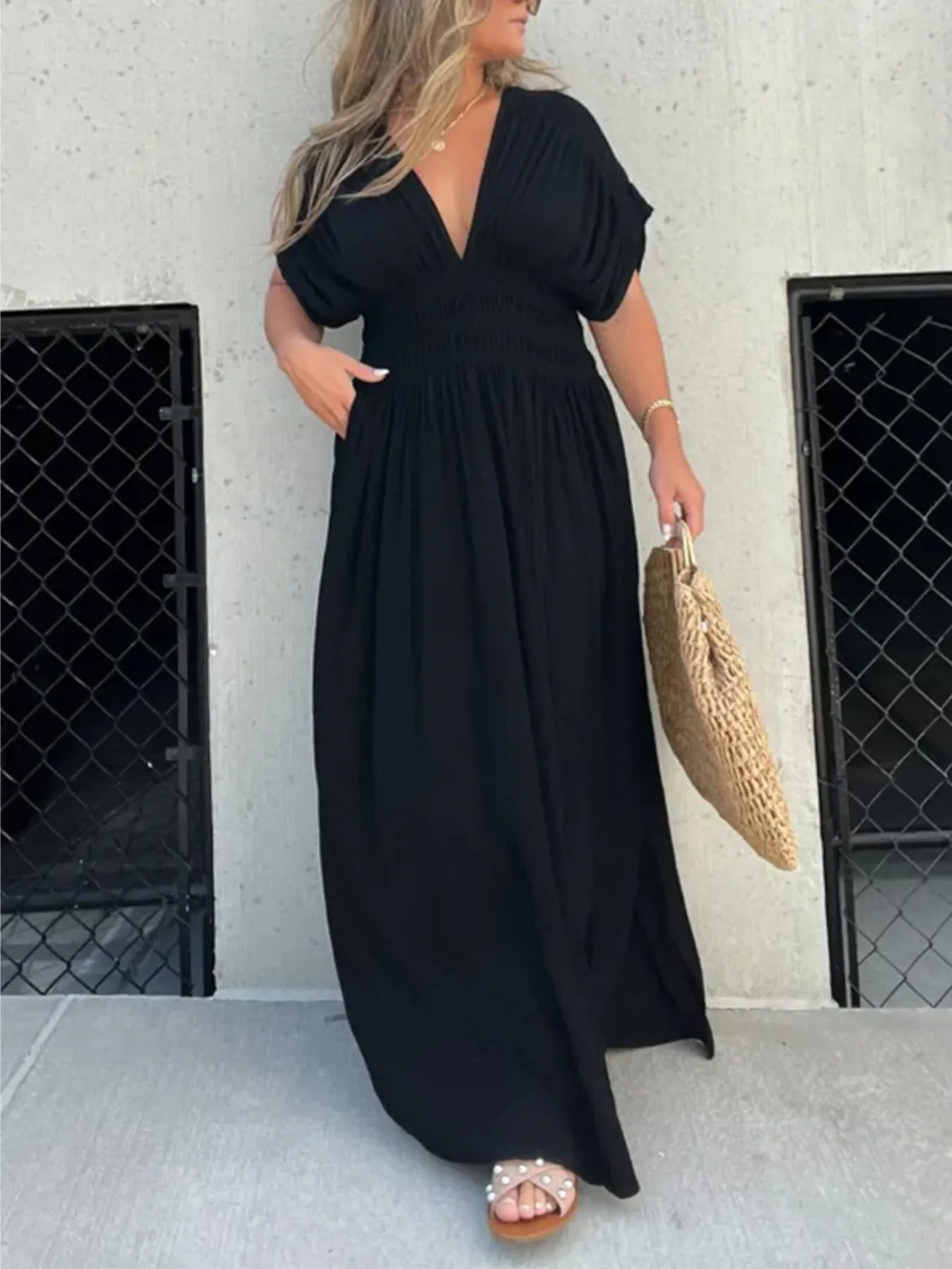 Woman wearing a flowing black deep V-neck maxi dress with side slit and relaxed elegant silhouette.